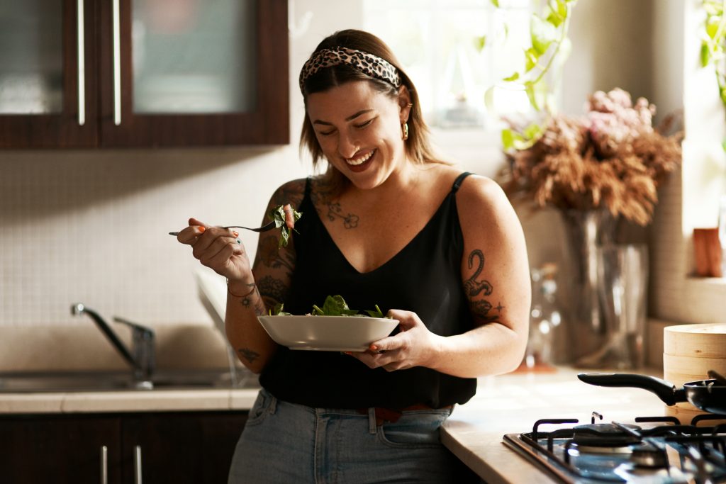 woman laughing and eating salad in kitchen