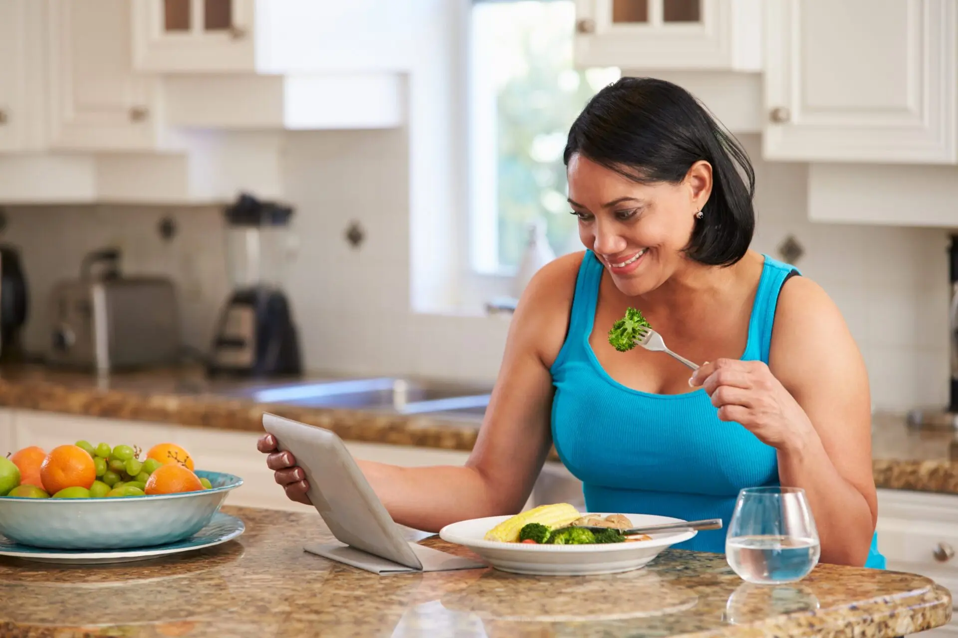 woman eating broccoli smiling at tablet
