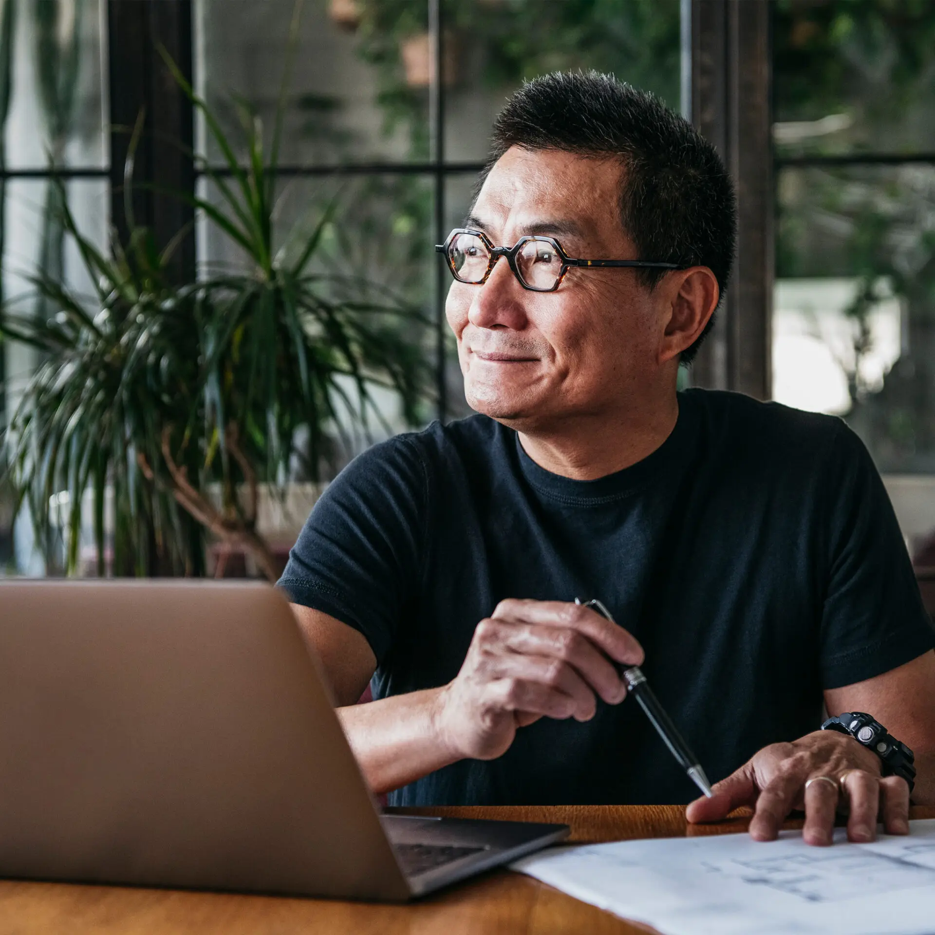 man with glasses using laptop at home looking out the window