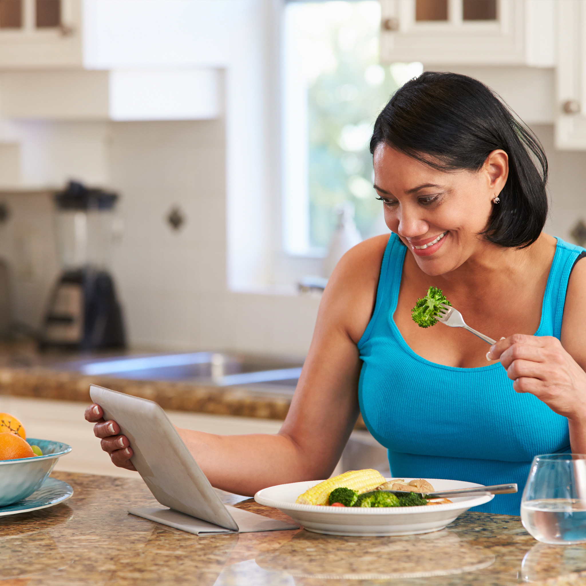 woman eating broccoli smiling at tablet