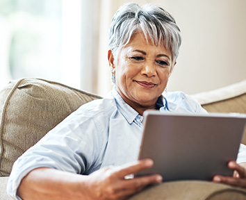 older woman sitting on couch smiling at tablet