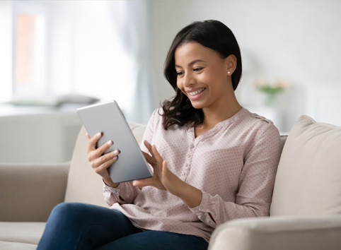 woman smiling on couch while looking at tablet