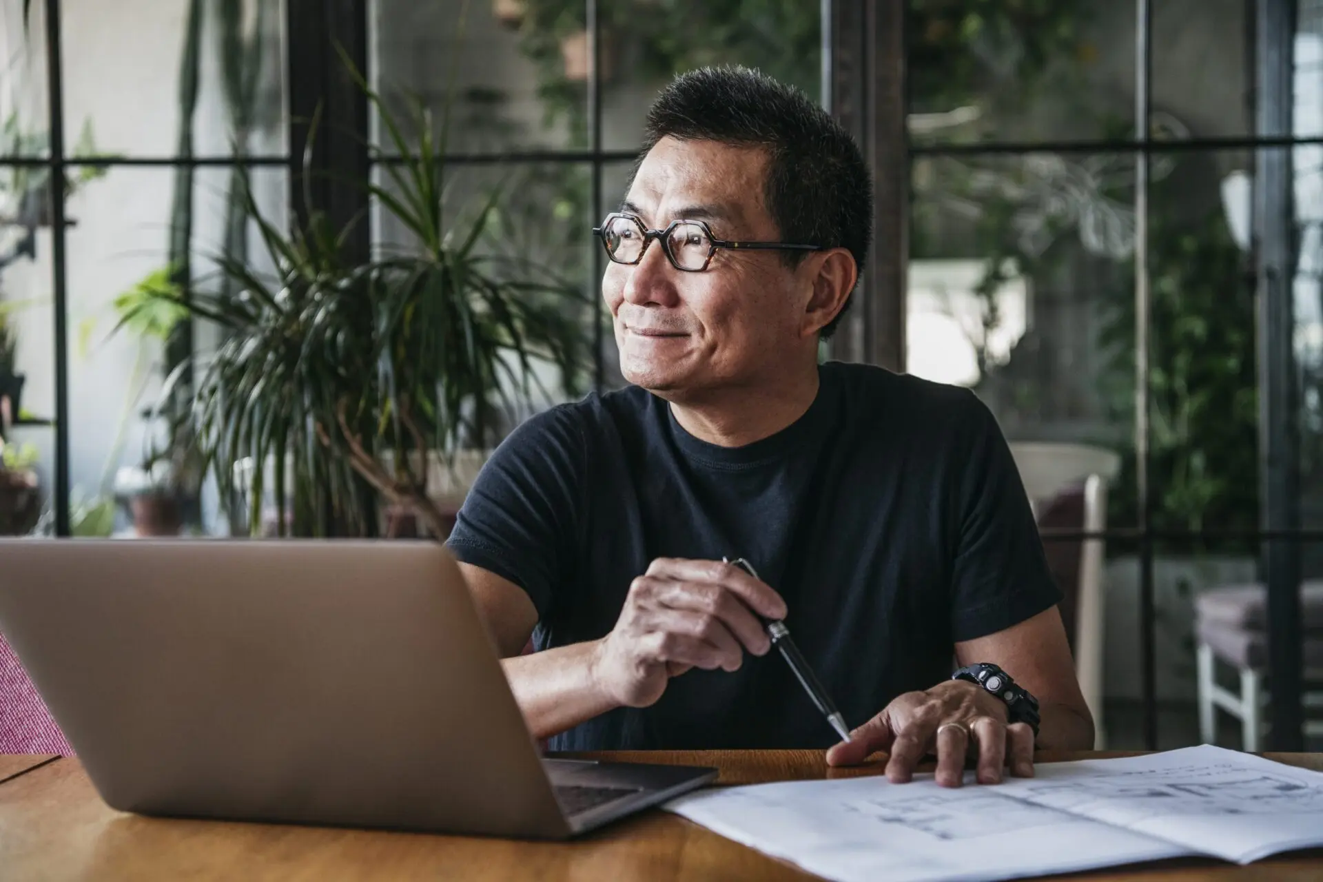man with glasses using laptop at home looking out the window