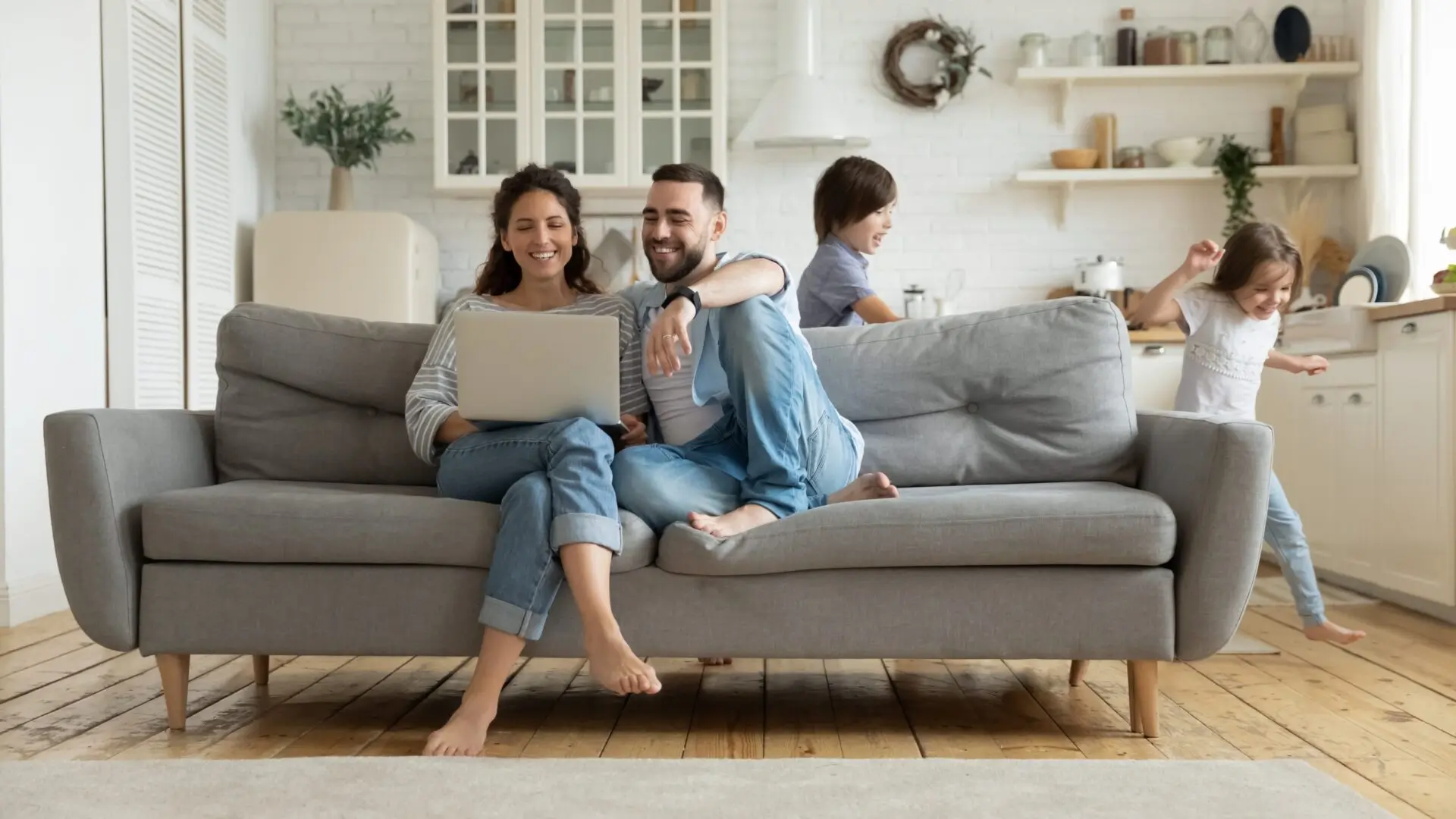 parents sit on sofa using laptop while kids run around