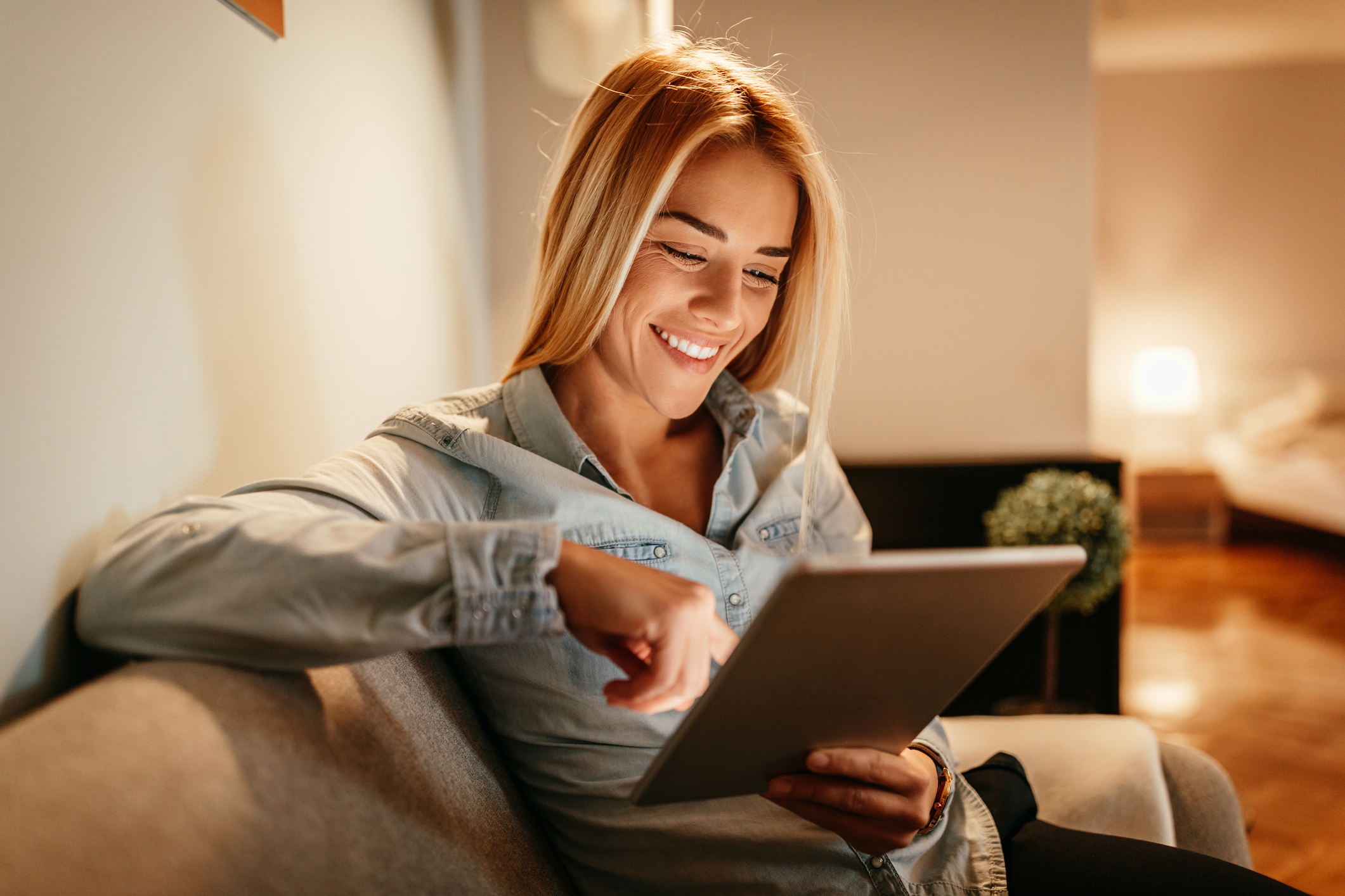 blonde woman smiling at tablet while scrolling screen at home