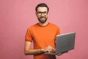 Man in glasses holding a laptop and smiling during a virtual coaching session.