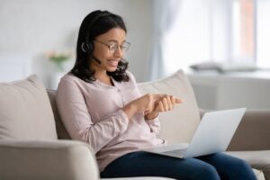 Woman in a headset smiling and interacting with her laptop during a virtual coaching session.