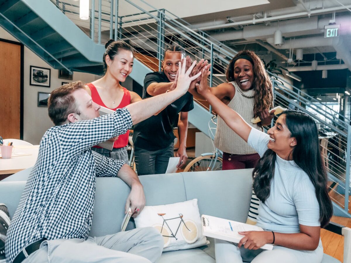 Diverse team of employees high-fiving in a modern office, celebrating a wellness program milestone