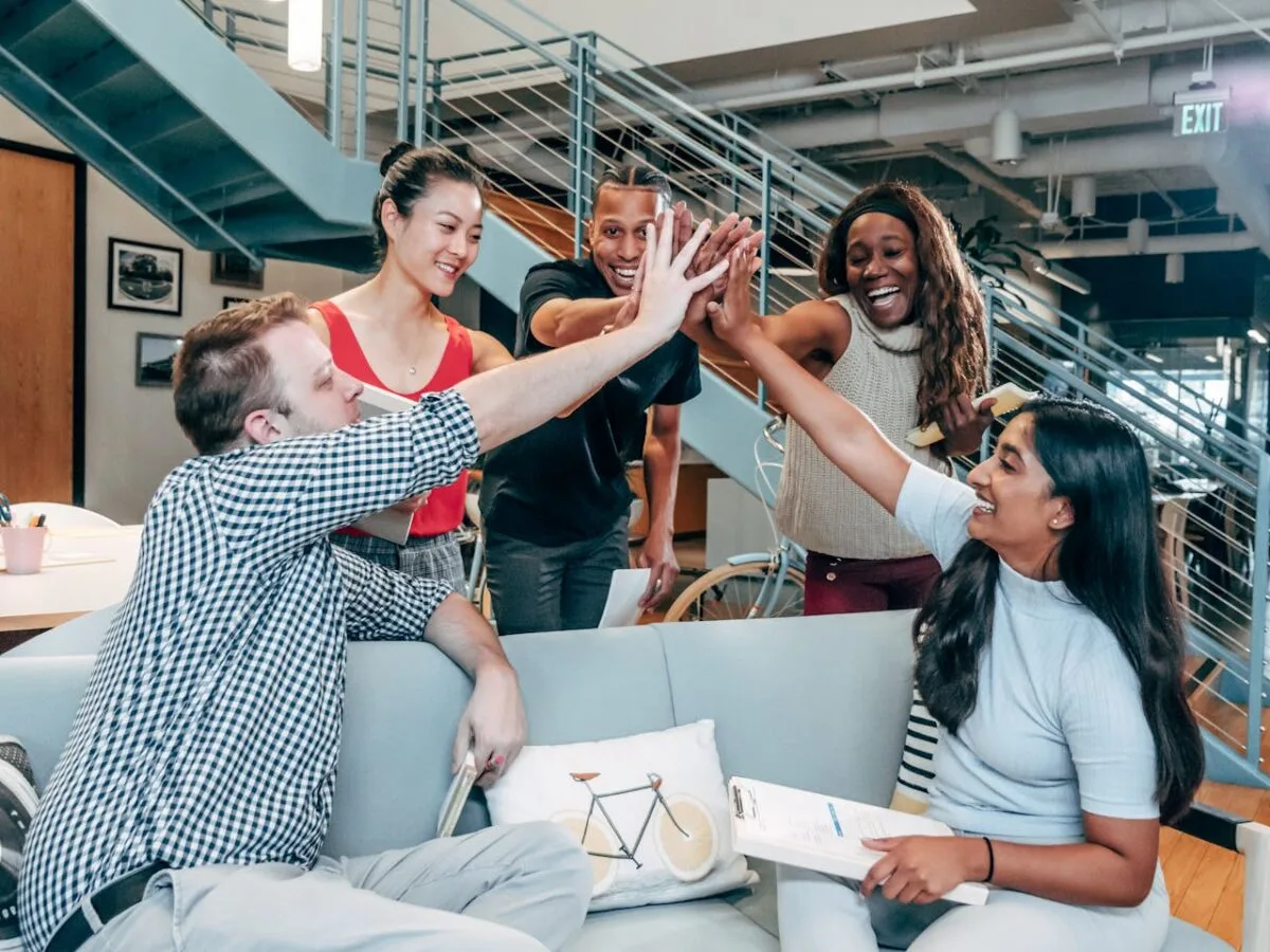 Diverse team of employees high-fiving in a modern office, celebrating a wellness program milestone