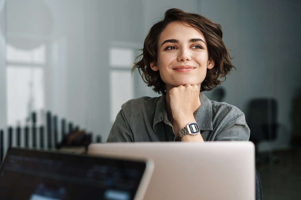 A smiling woman using a laptop, representing personal growth through digital health coaching and wellness tools.