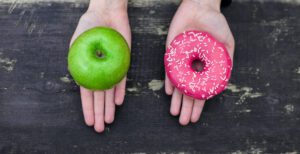 Case Study: Integrated Healthcare System Increased Health Coaching Engagement 4 Hands holding a green apple and pink donut, symbolizing choice between healthy and indulgent options