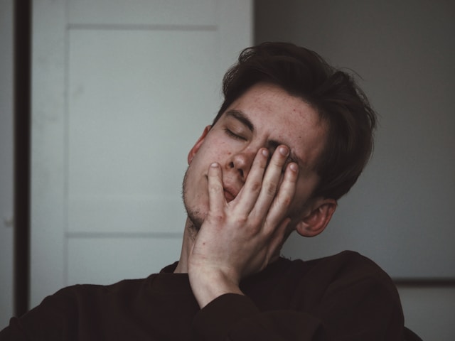 Young man resting his face in his hand, eyes closed, showing signs of exhaustion or frustration.