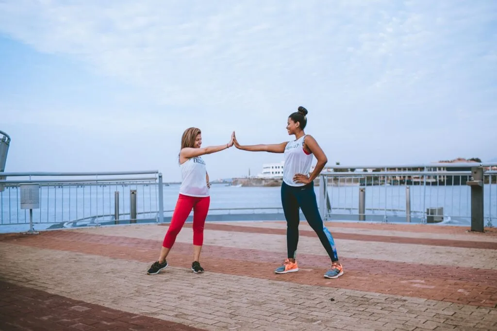 Two women high-fiving during an outdoor workout, symbolizing motivation and support from an accountability partner for fitness.