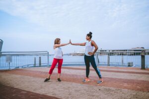 Two women high-fiving during an outdoor workout, symbolizing motivation and support from an accountability partner for fitness.