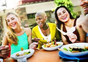 Diverse group of smiling adults sharing a healthy meal outdoors self care for busy parents