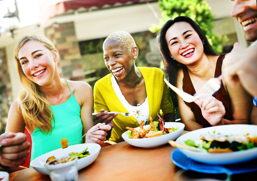 Diverse group of smiling adults sharing a healthy meal outdoors self care for busy parents