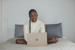 Woman sitting cross-legged on a bed using a laptop, creating a calm and flexible remote work environment.