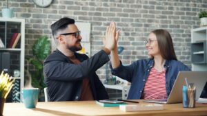 Two colleagues smiling and high-fiving in a modern office, celebrating collaboration and shared success.