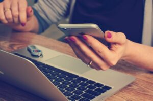 Employee multitasking on laptop and phone during the workday, representing the challenge of staff wellness in busy environments.