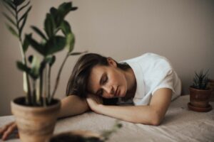 Tired woman resting her head on a table at home, surrounded by plants, capturing everyday sleep deprivation