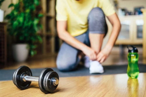 A person tying their sneakers next to a dumbbell and water bottle, symbolizing a small step in a consistent wellness habit.