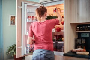 Woman choosing food from refrigerator during normal daily routine, showing how healthy eating habits happen in real life