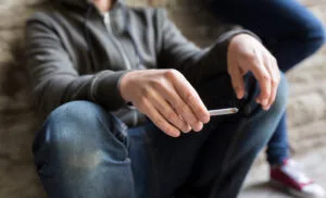 Person sitting outdoors holding a cigarette during a routine moment, reflecting real-life nicotine habits people try to quit.