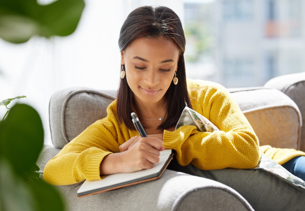 Woman writing in a journal while reflecting on her financial goals as part of a behavior change approach to financial wellness