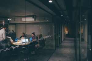 A small team works in a glass-walled conference room seen from a hallway, illustrating how vaping in the workplace often happens in plain sight but goes unnoticed by managers.