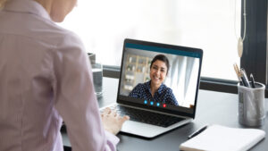 A health coach smiling during a video call on a laptop with an employee in a professional setting