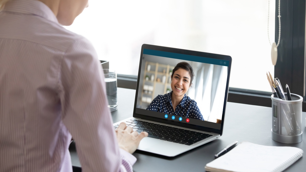 A health coach smiling during a video call on a laptop with an employee in a professional setting