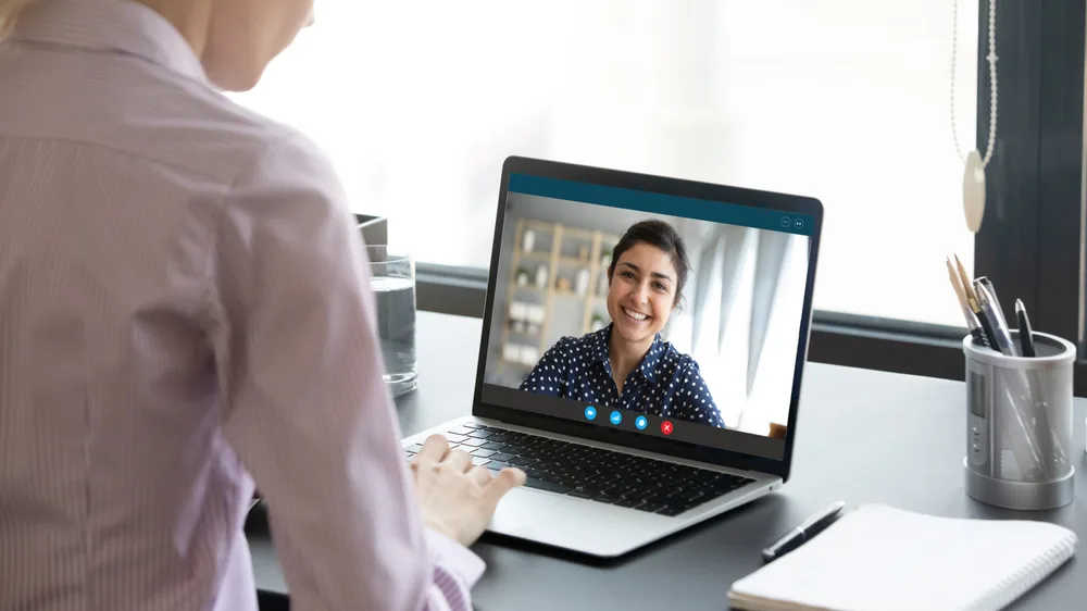 A health coach smiling during a video call on a laptop with an employee in a professional setting