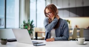 Woman at her desk rubbing her neck in pain, illustrating workplace musculoskeletal pain and employee absenteeism