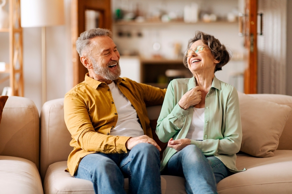 Older couple laughing together on a couch, staying socially connected