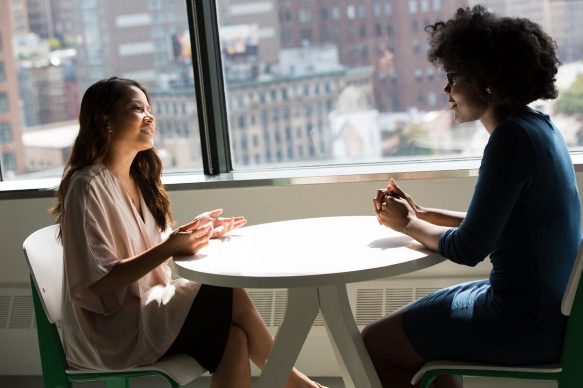 Two coworkers having a supportive one-on-one conversation at a sunlit office table, illustrating workplace grief support