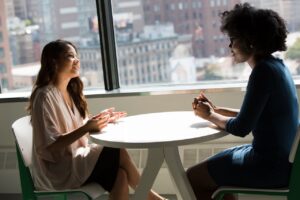 Two coworkers having a supportive one-on-one conversation at a sunlit office table, illustrating workplace grief support