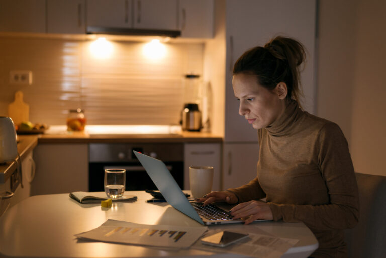 Employee reviewing benefits paperwork and a laptop at her kitchen table during open enrollment