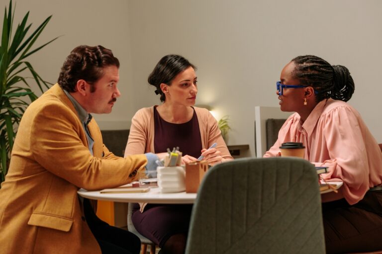 Three coaching program leaders in discussion around a small office table during a client outcomes review