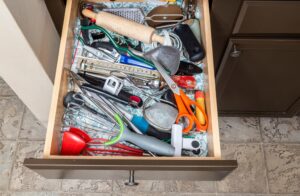 Overstuffed kitchen drawer crammed with utensils including a rolling pin, grater, scissors, ladles and spatulas