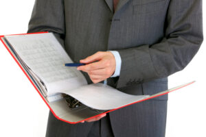 Person in a suit reviewing printed standards in a red ring binder with a pen