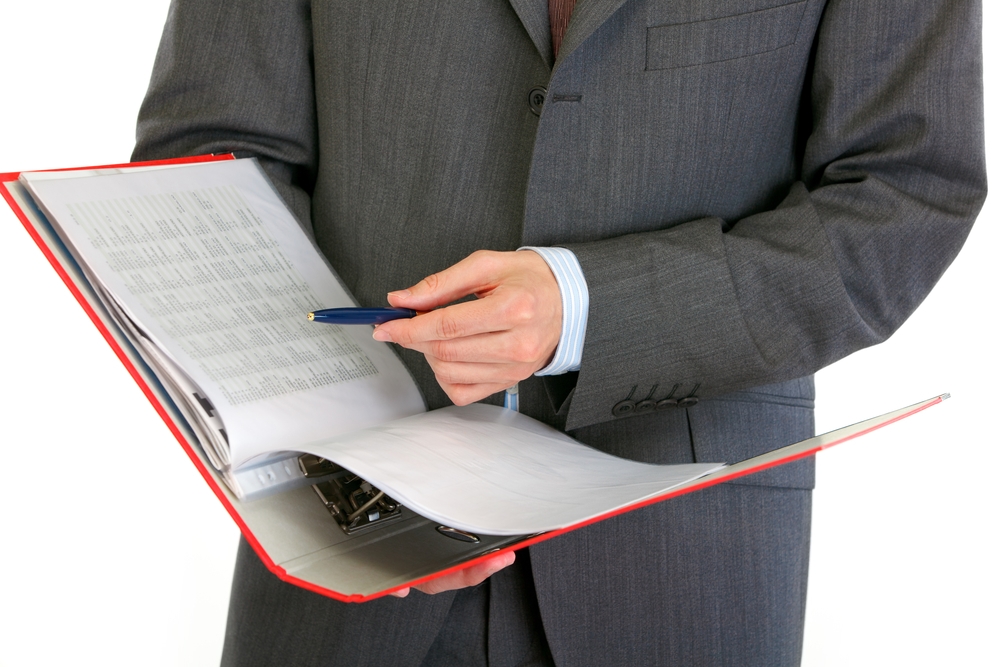 Person in a suit reviewing printed standards in a red ring binder with a pen