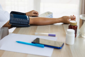 Person checking their blood pressure at home with a cuff, phone and notepad on the table