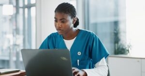 Nurse in scrubs reviewing patient information on a laptop in a clinic office