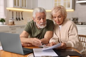 Older couple at a kitchen table reviewing plan paperwork together