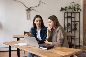 Two health coaches at a wooden table reviewing a coaching session together on a laptop