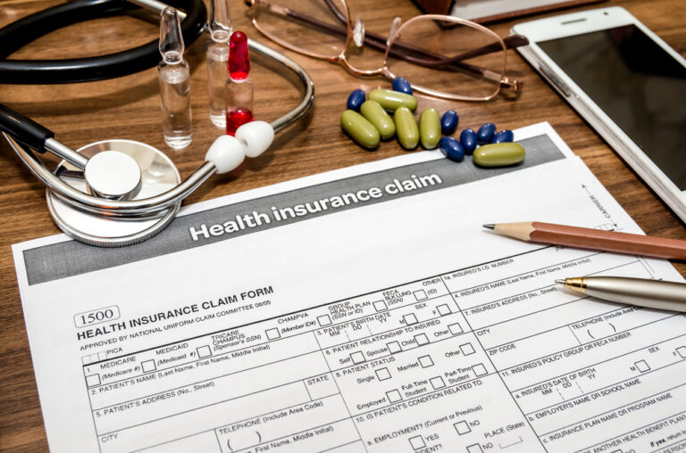 Health insurance claim form on a desk with a stethoscope, pills, glasses, a phone and a pen