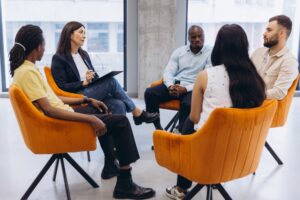 A health coach with a clipboard leading a small group of adults seated in a circle