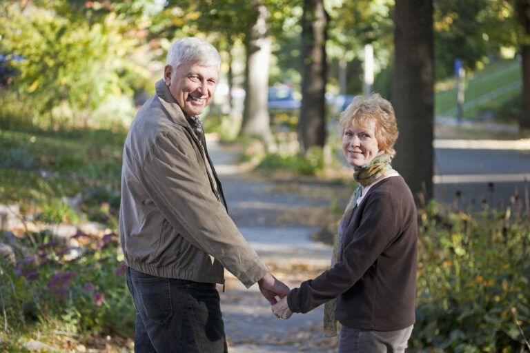 Older couple holding hands on a tree-lined sidewalk in autumn