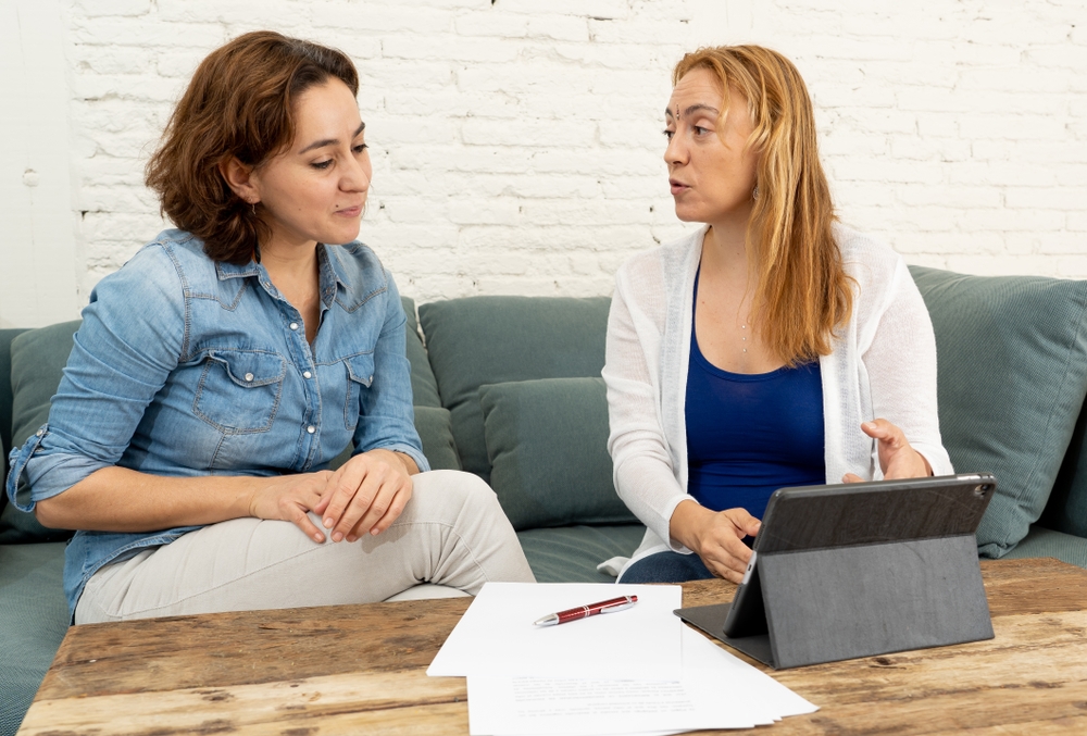Two women in a bright office discussing papers spread on a low table
