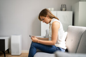 Woman sitting on a couch hunched forward over her smartphone, showing tech neck posture